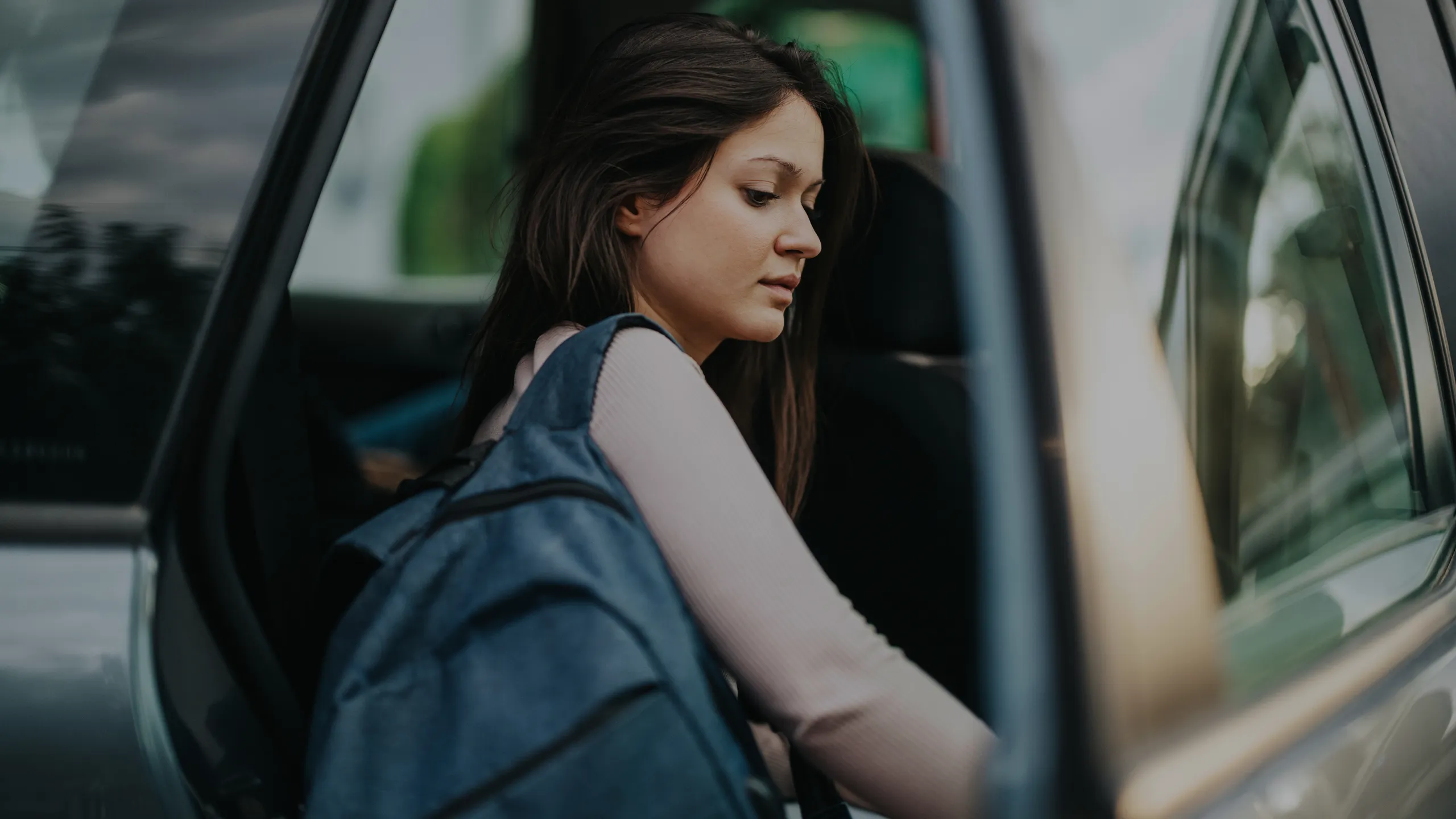 Young girl getting out of car with backpack at school drop-off