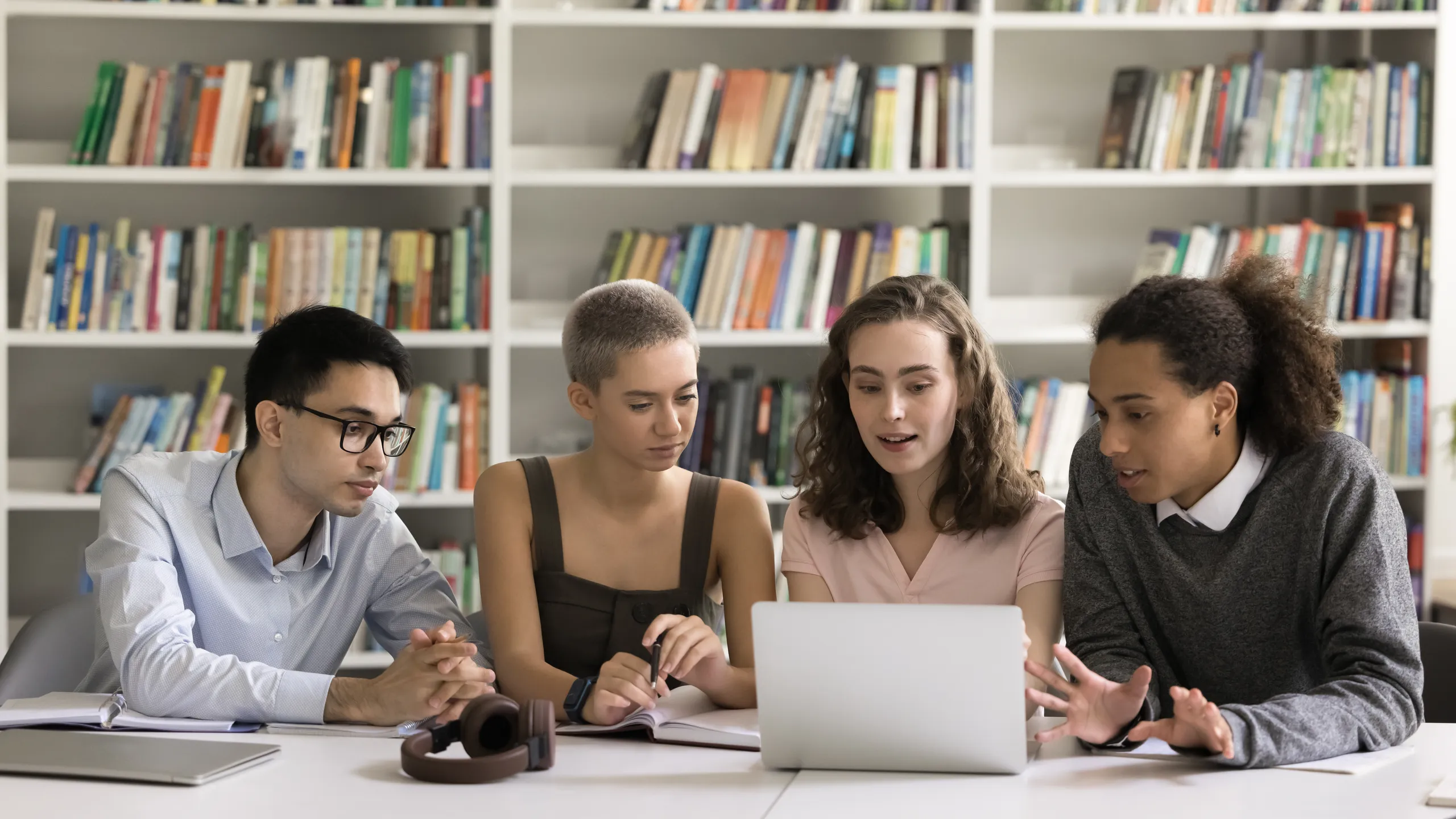 Four diverse multicultural schoolmates using laptop in learning at library