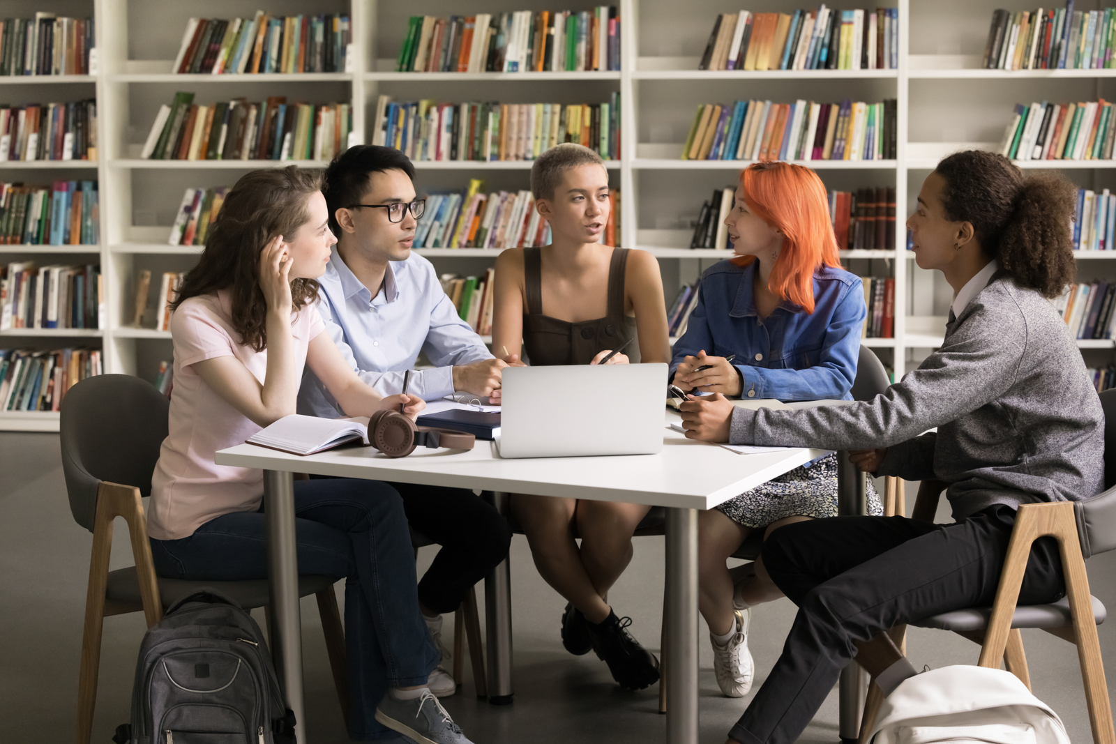 Multiethnic teenage students gather in library around table with laptop