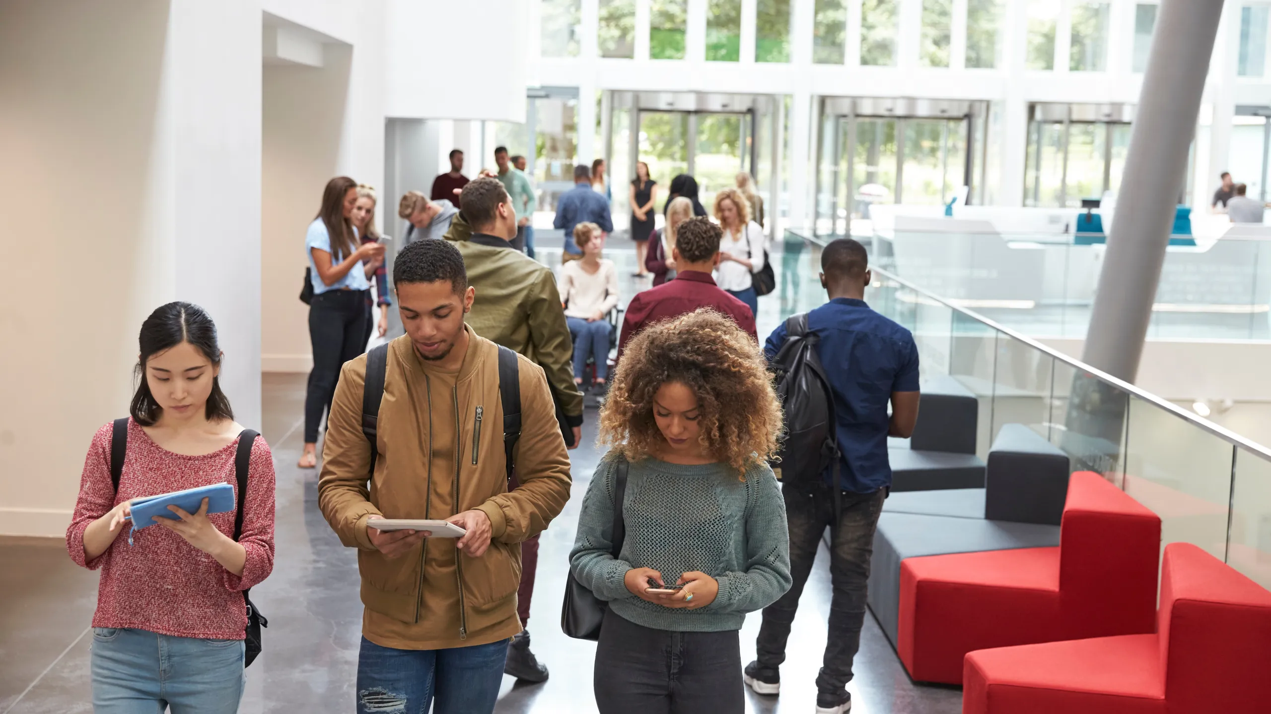 Students walk in university campus using tablets and phone