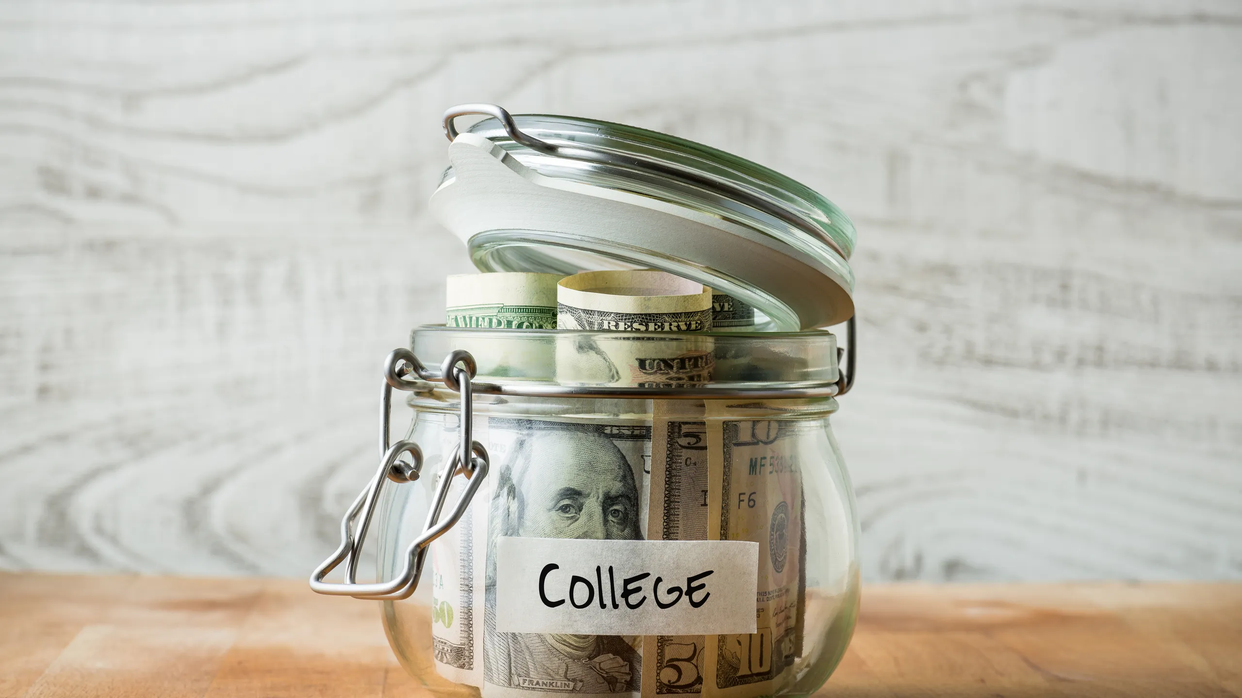 Dollar bills in glass jar isolated on wooden background. Saving