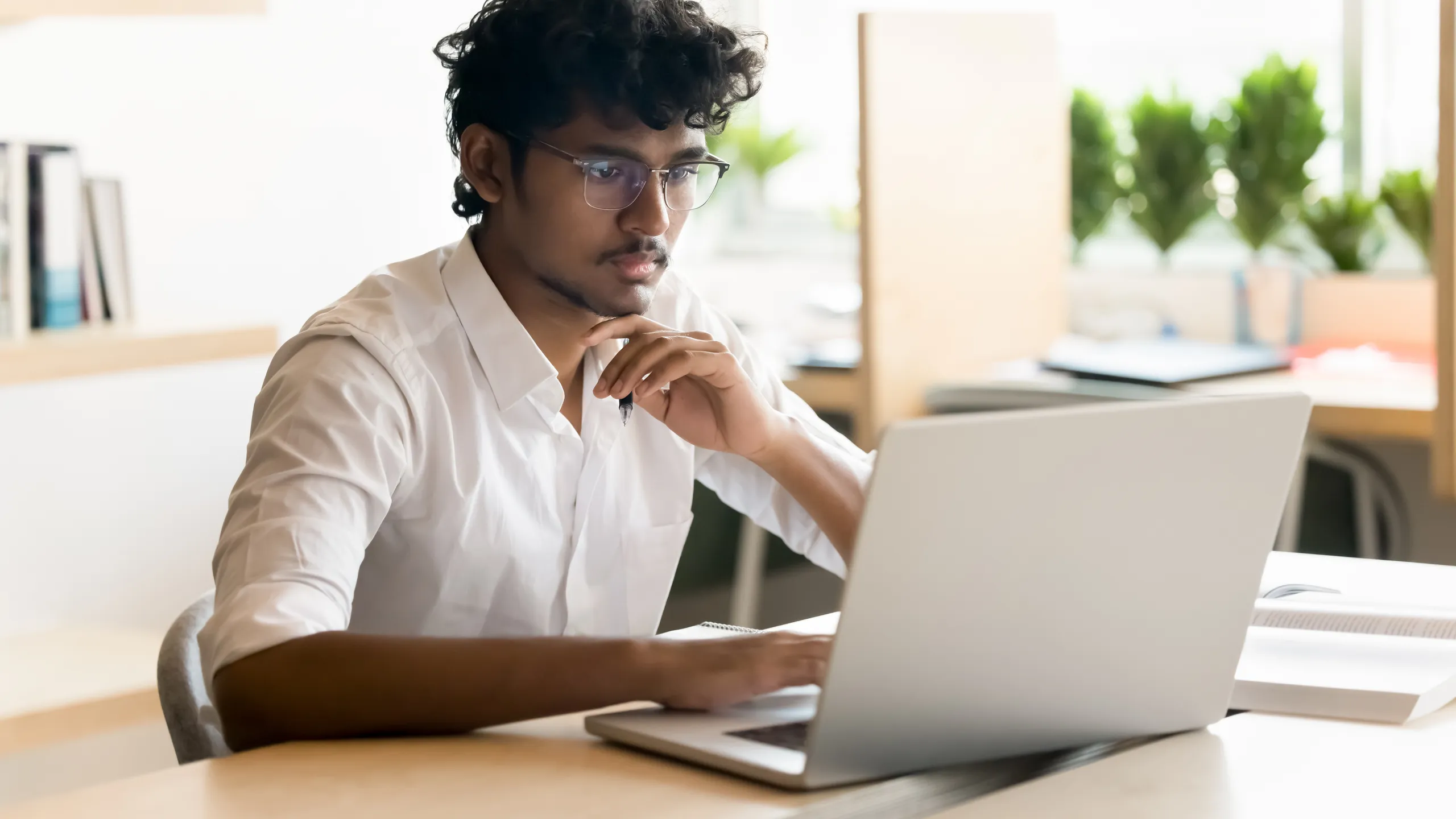 Young man in glasses sit at office desk using notebook