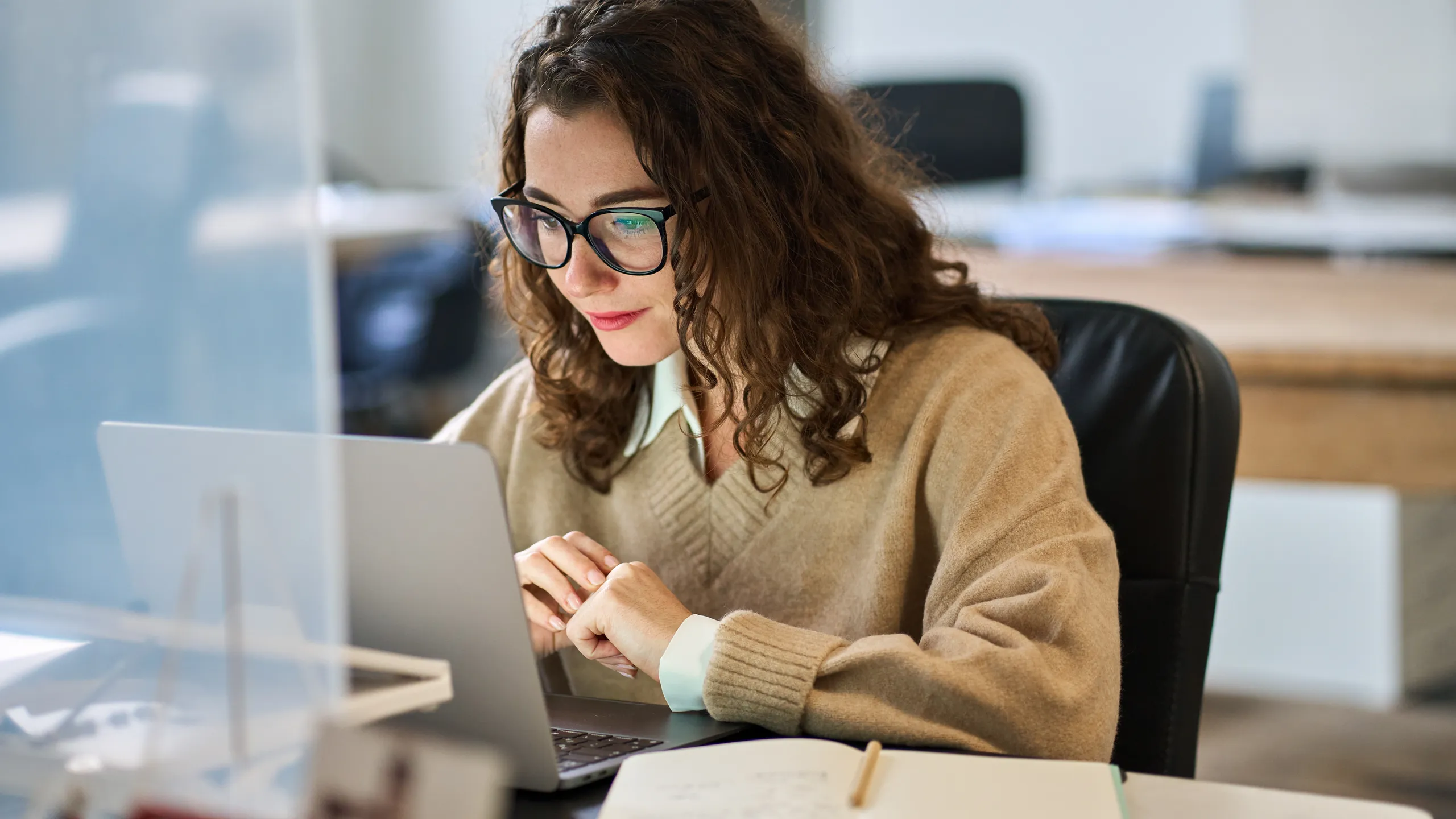 Young woman worker wearing glasses watching online webinar at work.