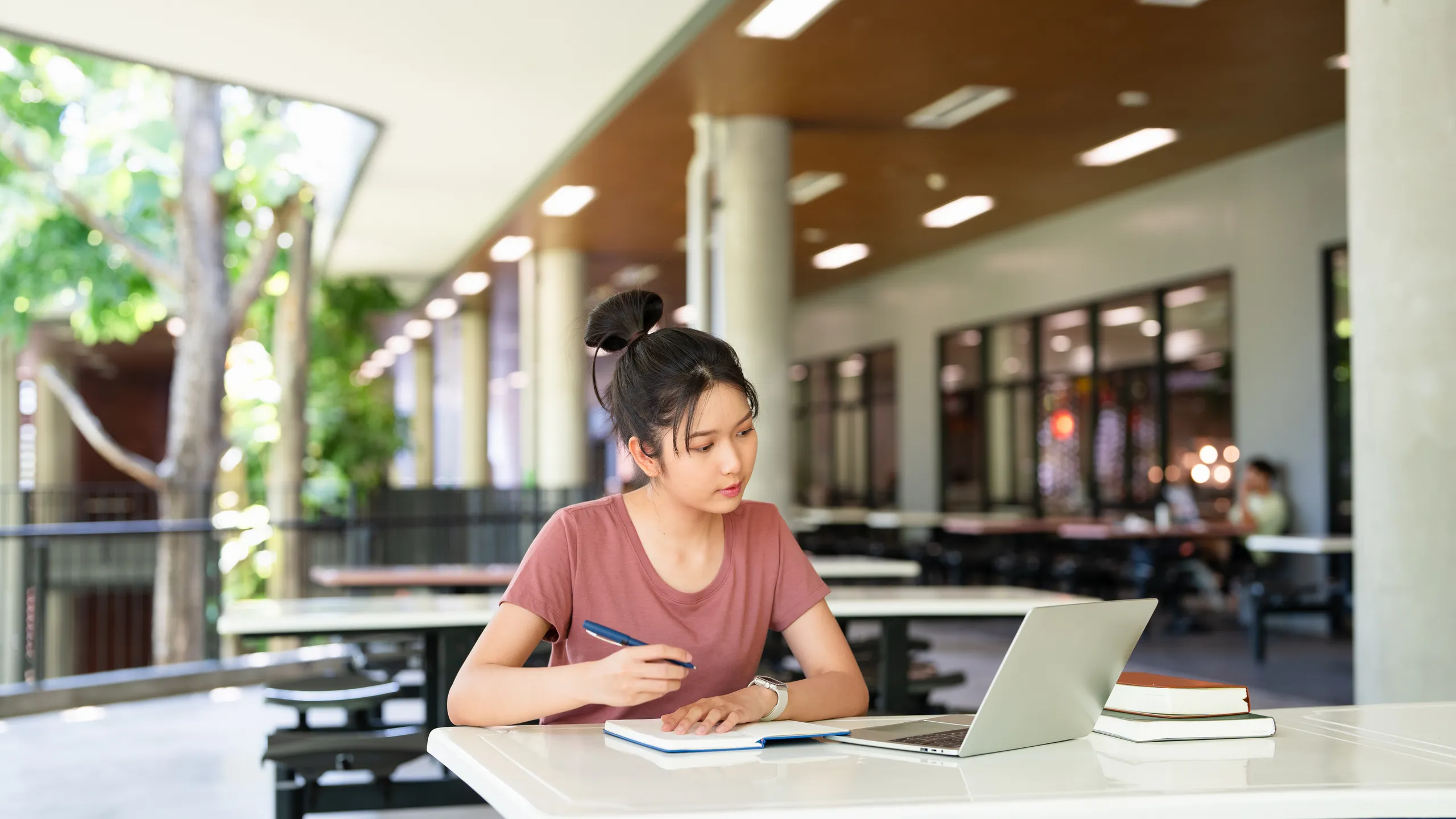 Focused asian teen girl student writing notes in notebook distance learning studying online makes goals check list at cafeteria. college school education, elearning concept.