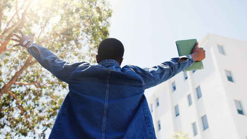 Man, student and tablet in city with freedom, academic achievement or scholarship opportunity. Back, low angle or person outdoor with tech for university acceptance, success or funding grant to study