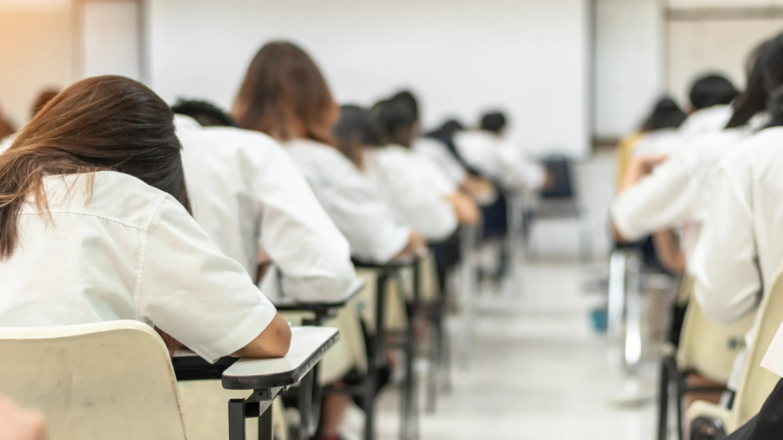 School student exam in university class with blurry view from back of the classroom of young people having stress doing examination admission test in classroom for education background