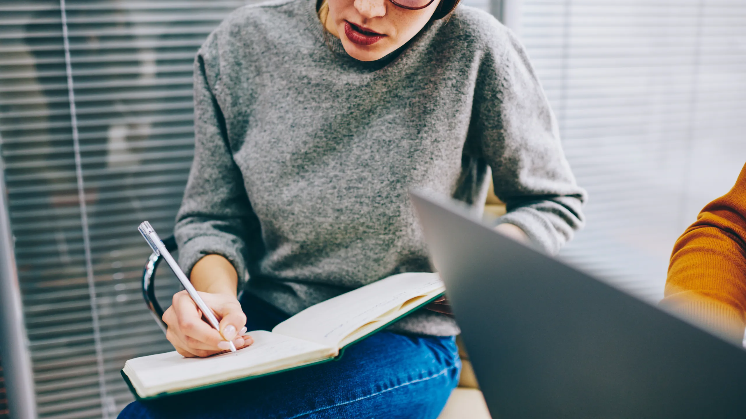 Copped view of pensive young woman in eyeglasses writing down essay in notebook doing homework.Smart concentrated hipster student making notes in notepad preparing for upcoming exams