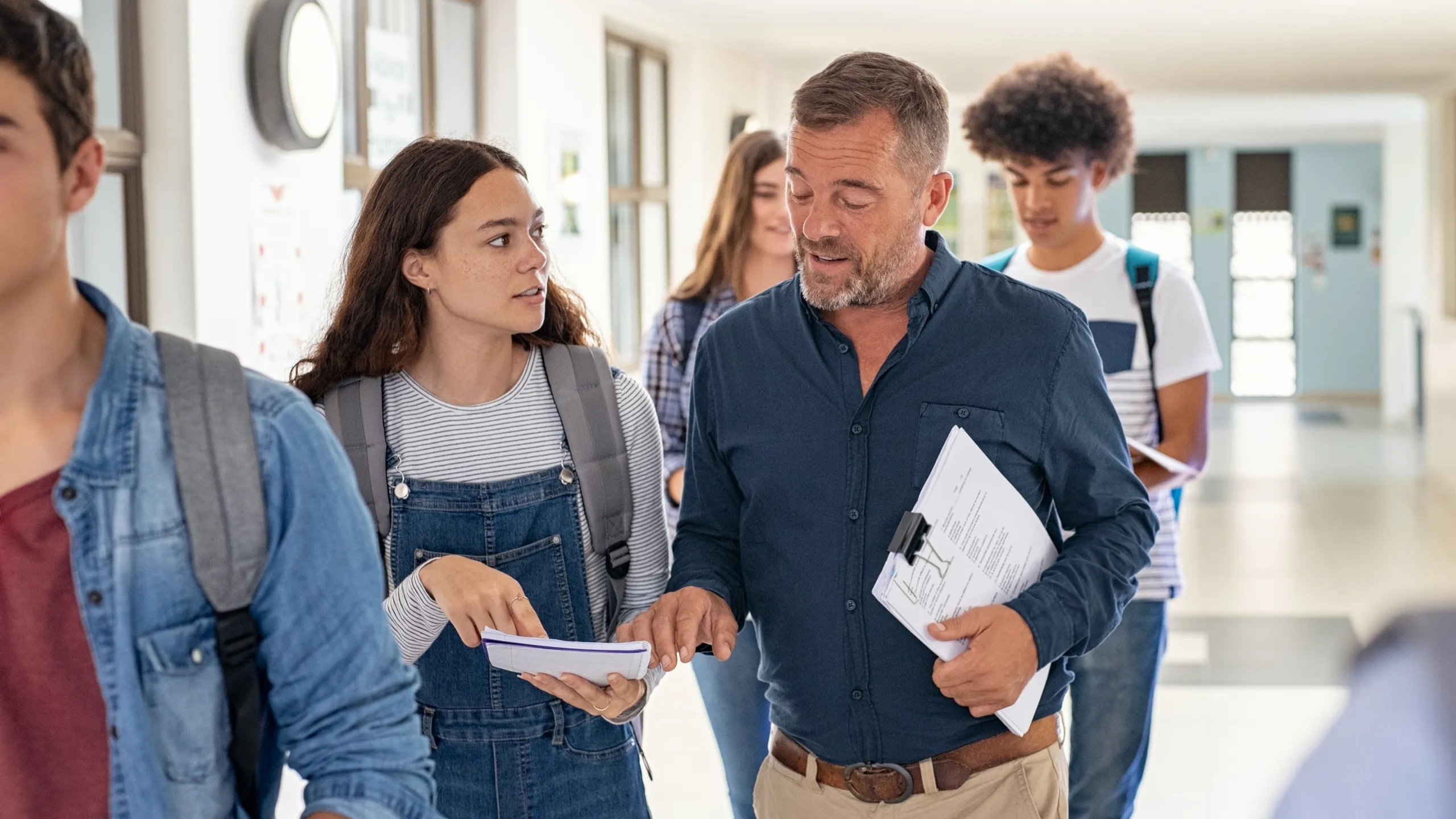 College girl talking to teacher in school hallway