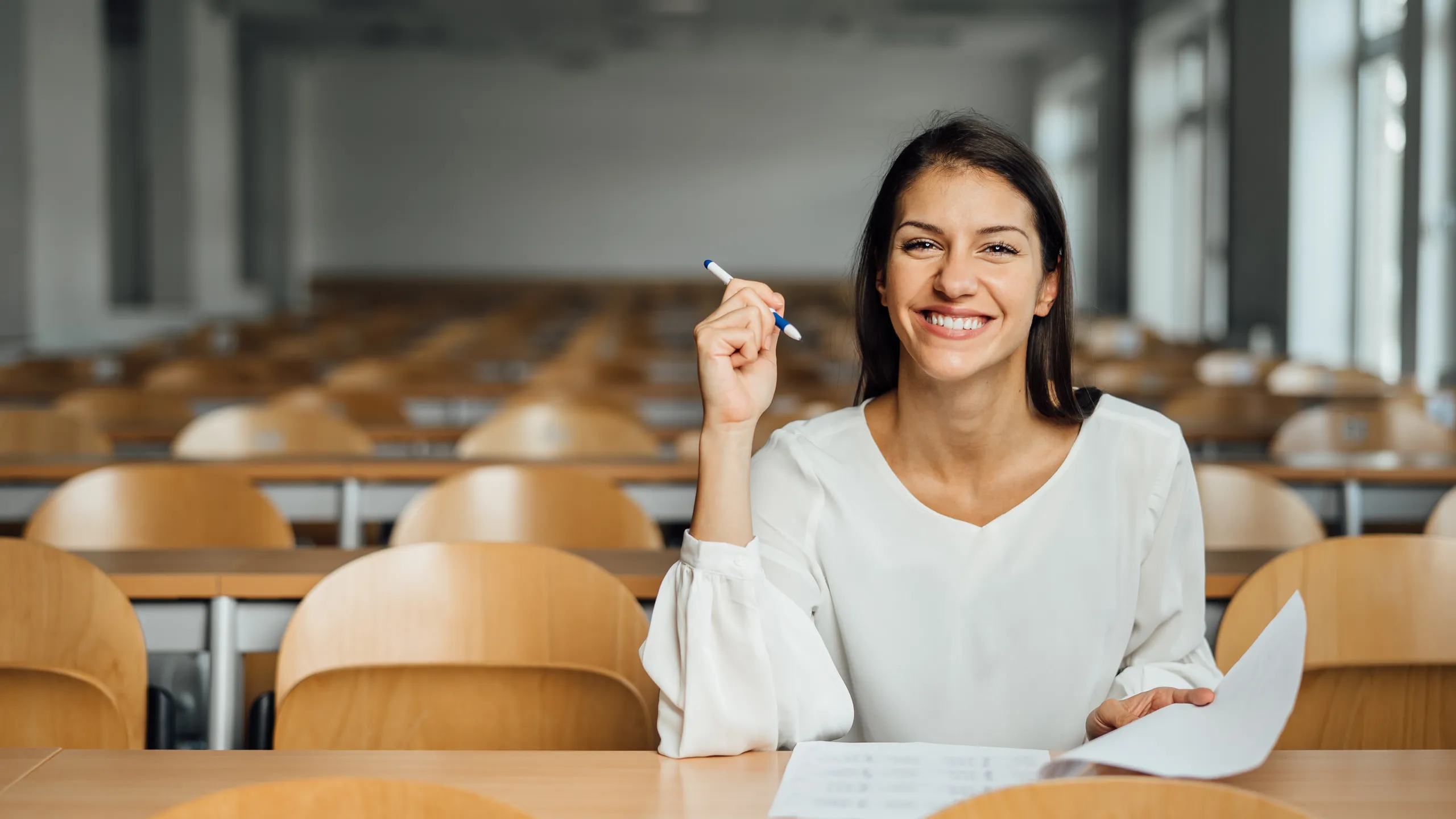 Knowledgable smiling student taking an easy exam in an empty amphitheater. An optimistic student taking an in-class test. Happy woman having stress free education evaluation.Essay exam inspiration.