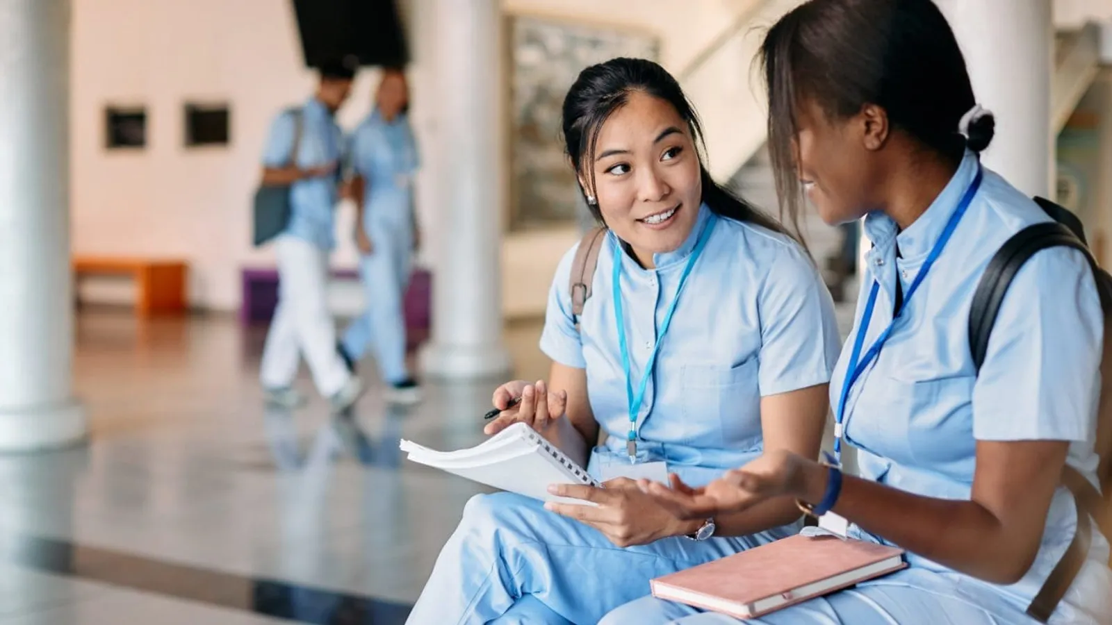 Nursing student and her female friend talk while studying in hallway at medical university.
