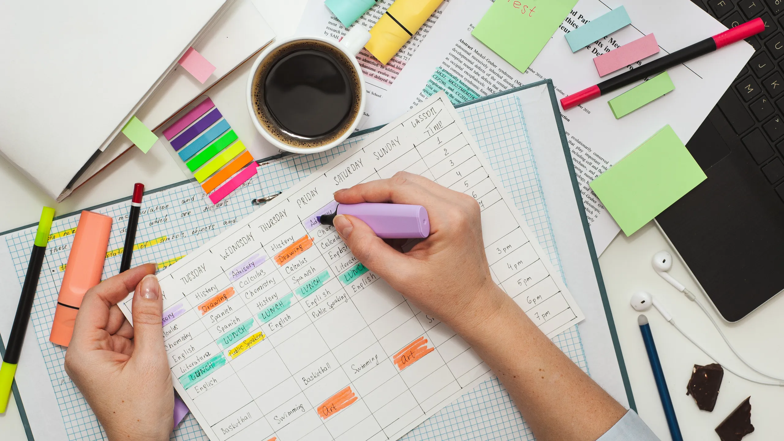 Student desk. The girl makes notes on stickers in the study schedule. The process of homeschooling or preparing homework . Top view of the table with student stationery and notes.