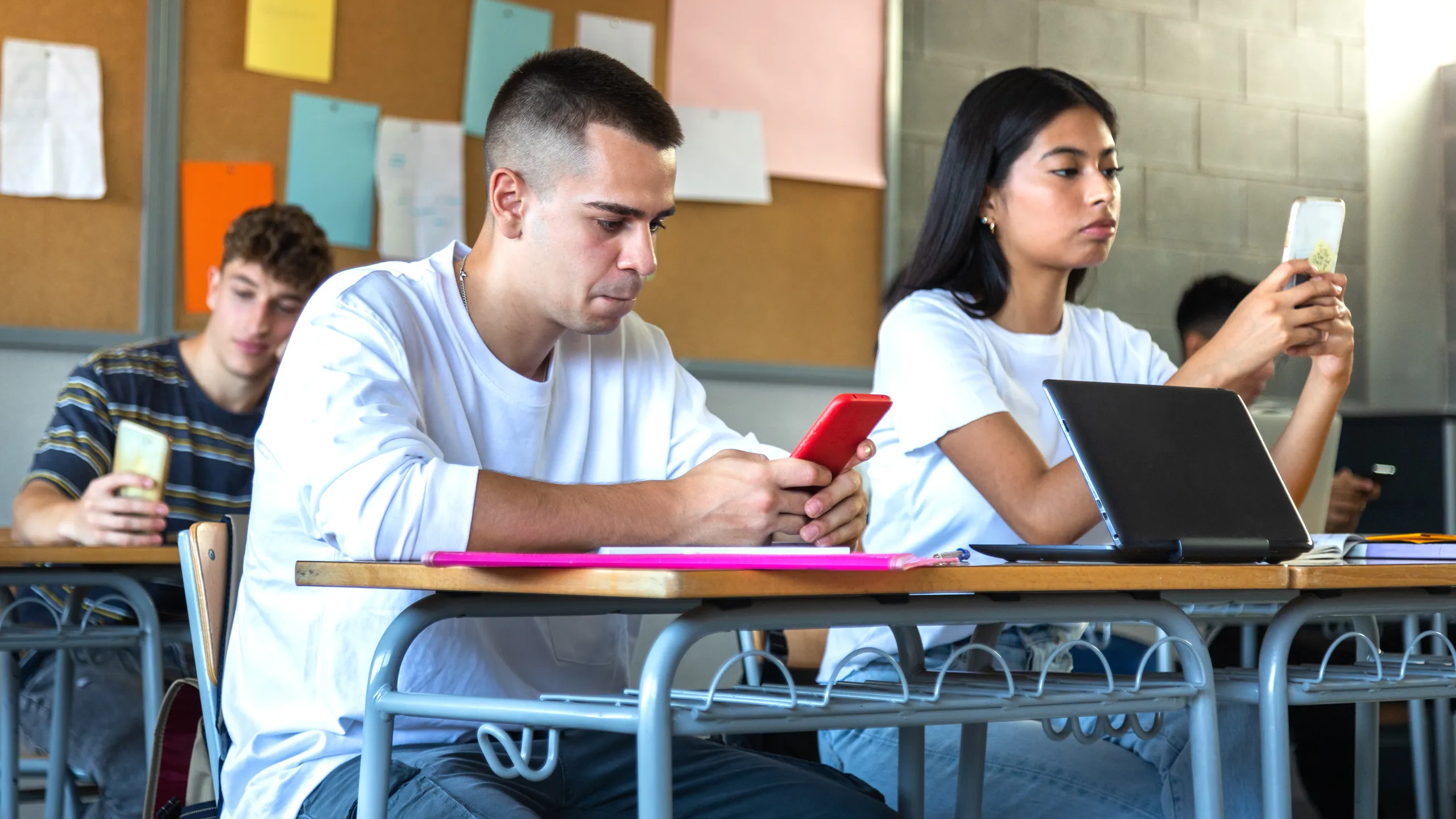 Diverse teenage high school students using phone in class to text message, use social media apps and take selfies.