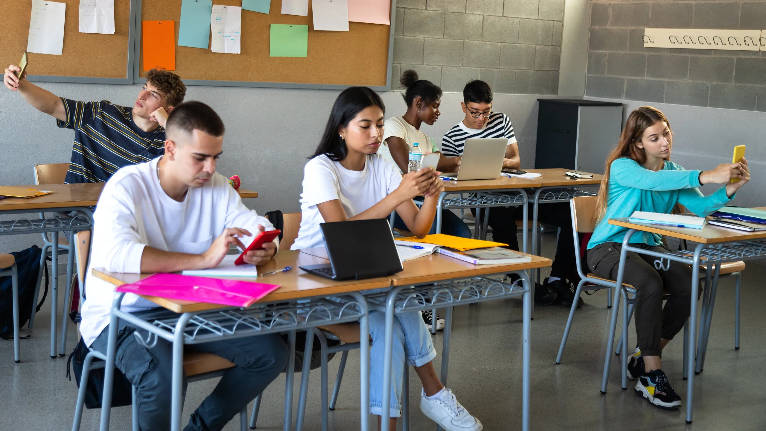 Multiracial high school students using phone in class to text message and take selfies no interacting with each other.