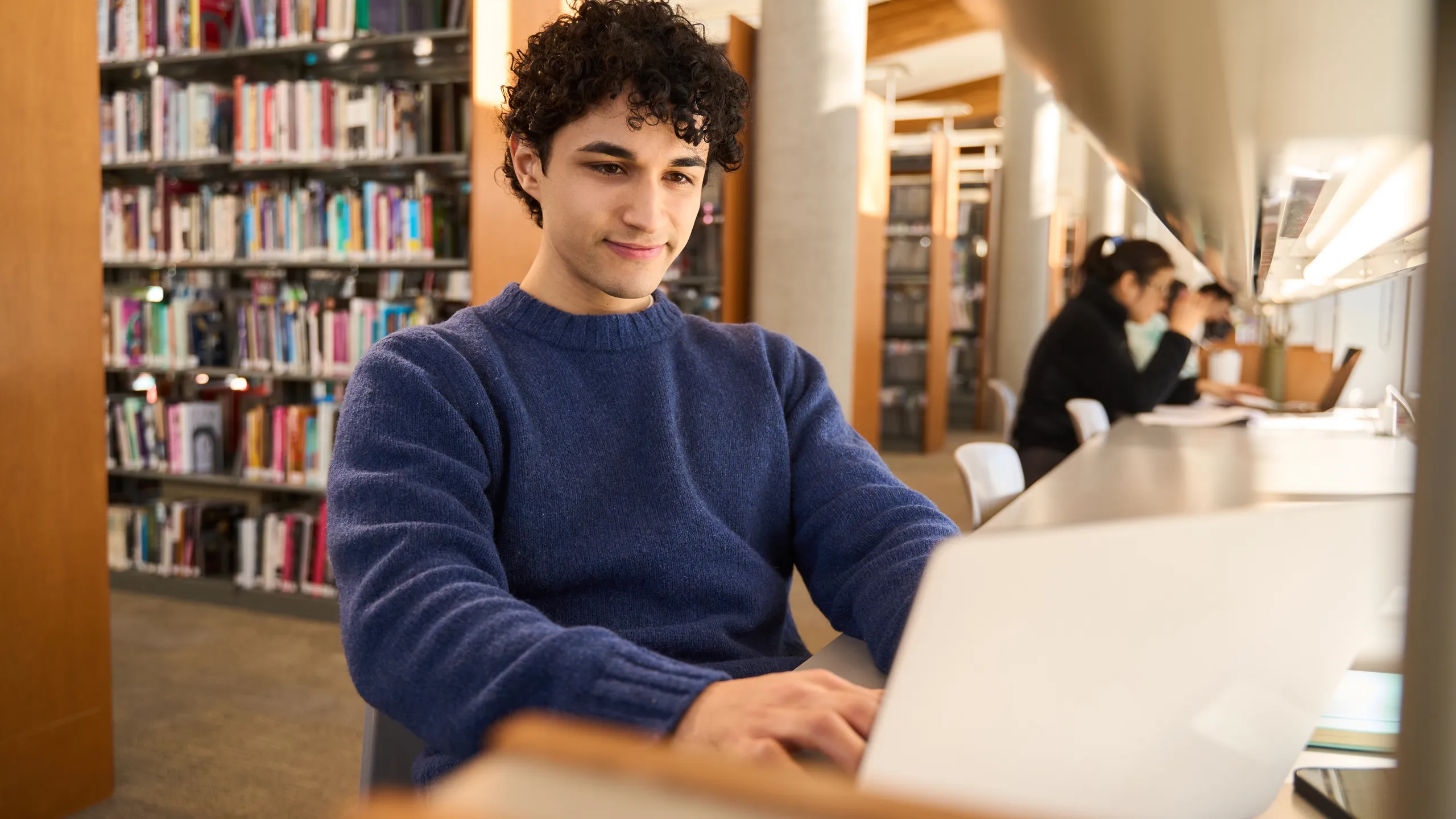 Latin American male student using laptop, making researches on internet in modern innovation library