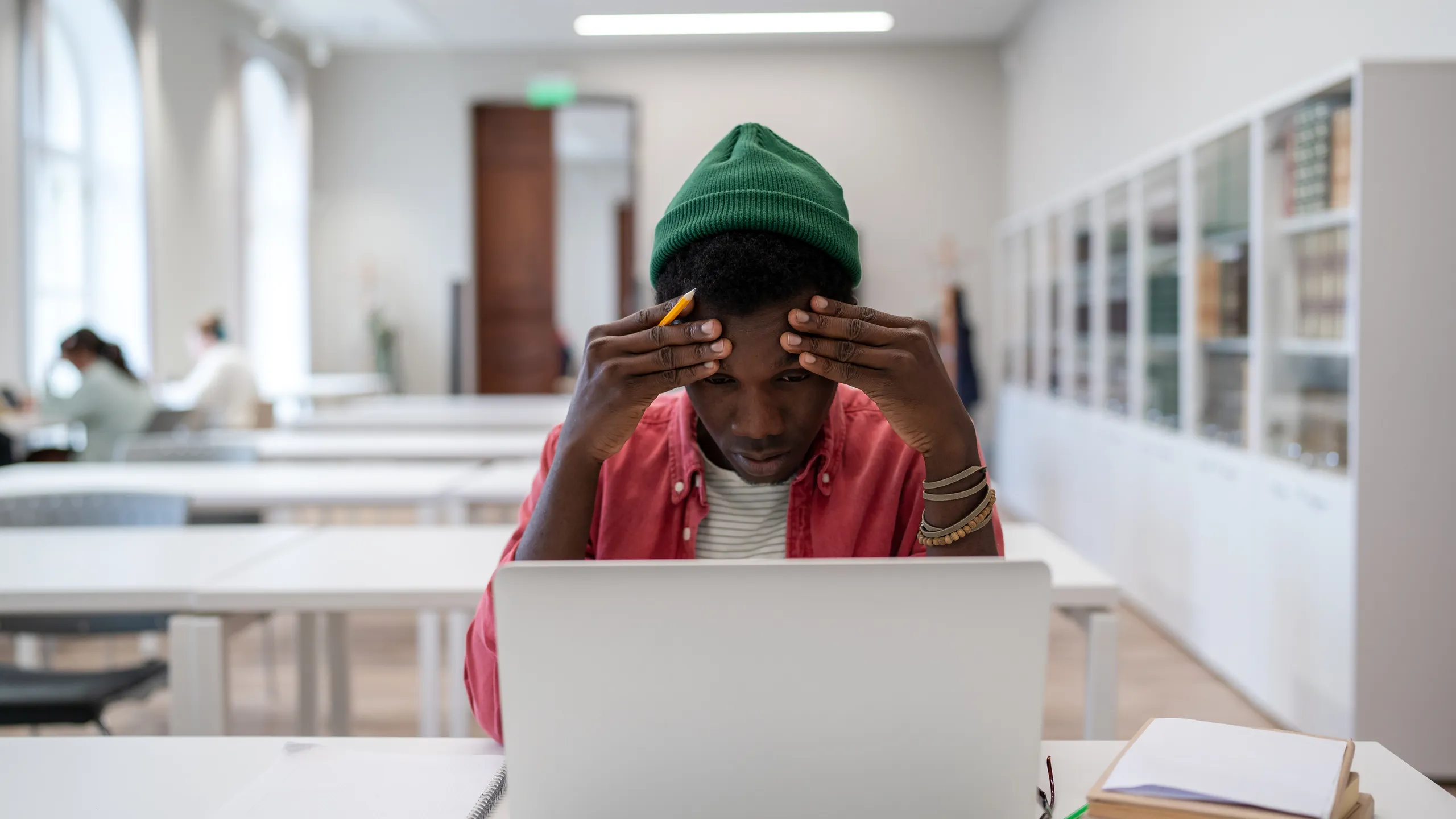 Exhausted mixed race student man touch head feel migraine after laptop study in university library