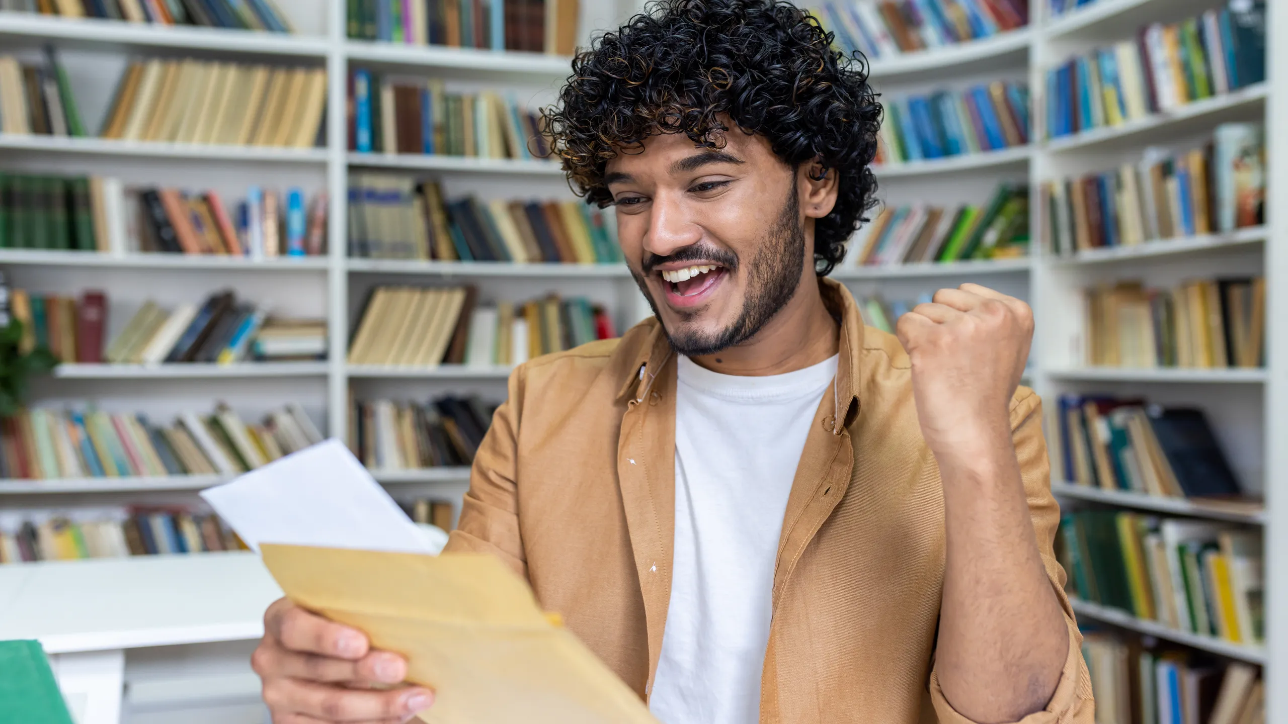 Young student received letter with good exam results and university admission confirmation, hispanic man with curly hair celebrating successful achievement holding hand up close up