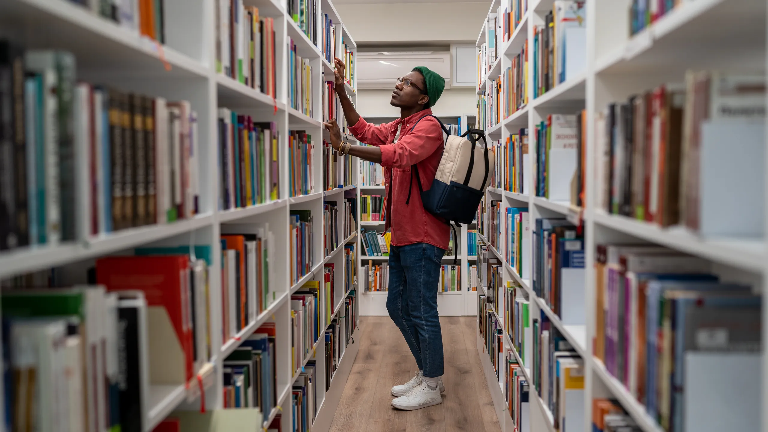 Thoughtful African American student man in glasses choosing book in college library or bookstore