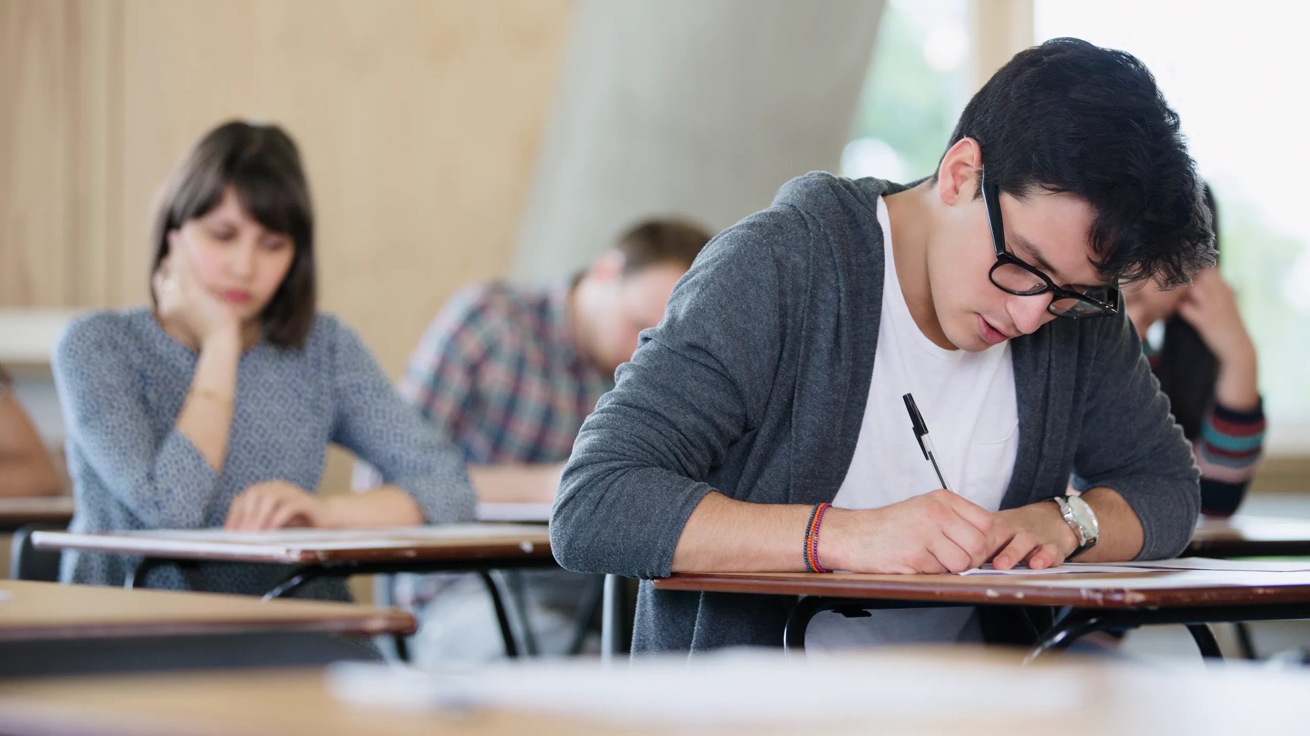 Focused male college student taking test at desk in classroom