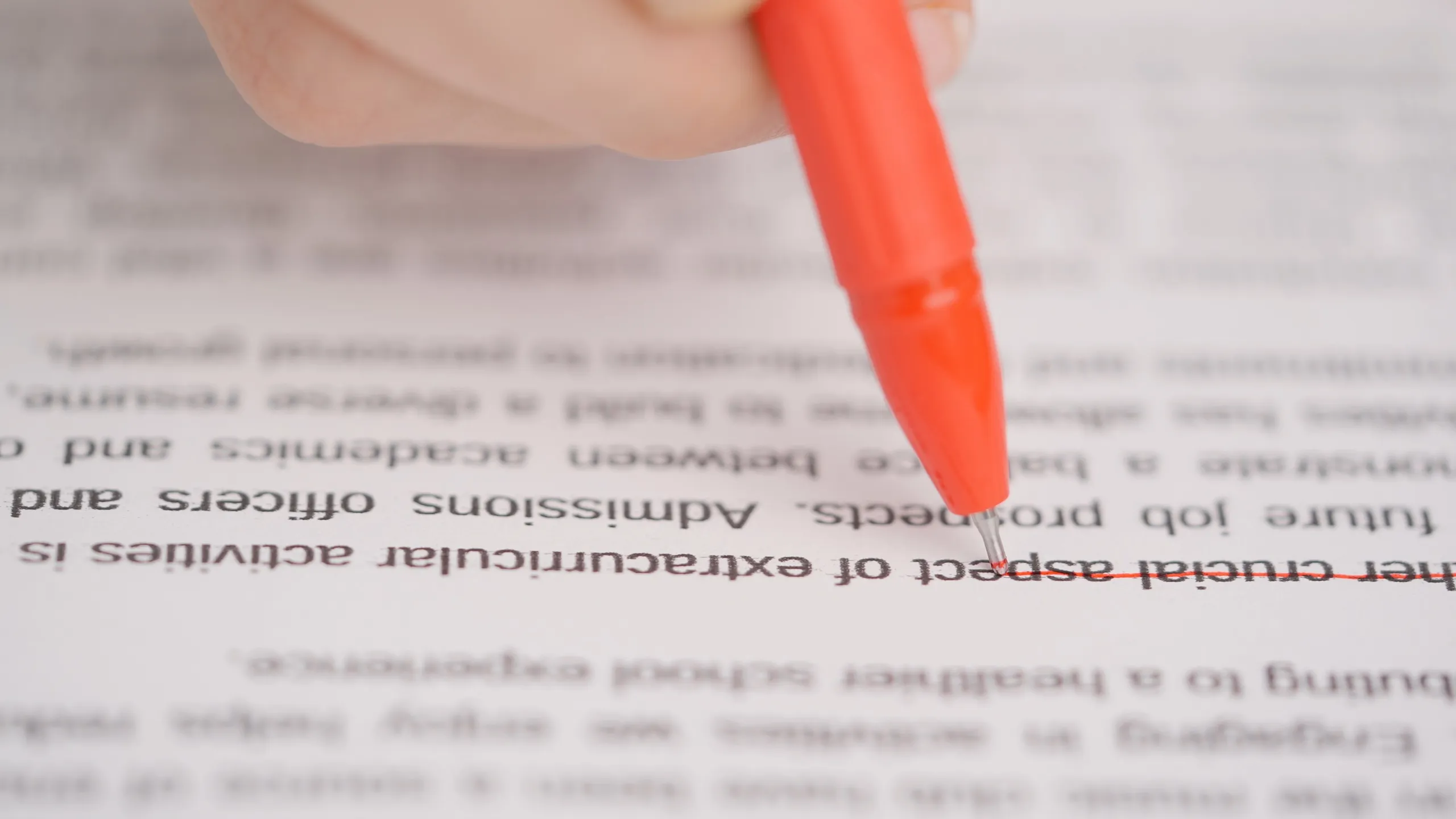 Professional school or college teacher grades a homework exam papers of students. Woman checks essay, crosses wrong sentences with red pen.