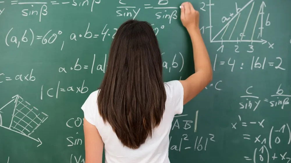 Clever-young-woman-solving-a-mathematical-problem-standing-with-her-back-to-the-camera-writing-on-a-college-blackboard