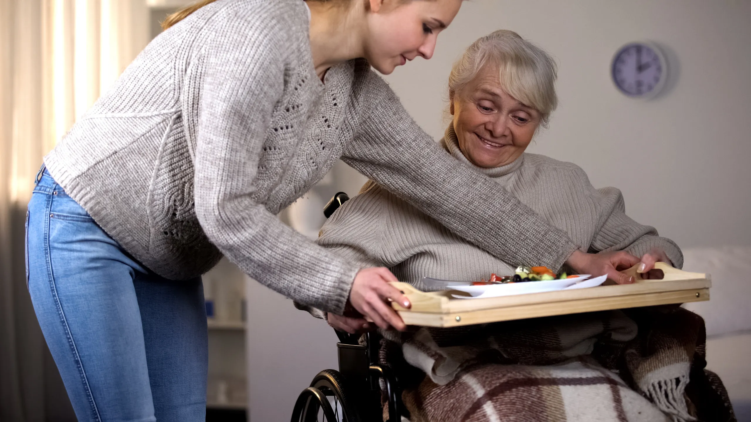 Female volunteer serving dinner to handicapped old woman, elder care, help