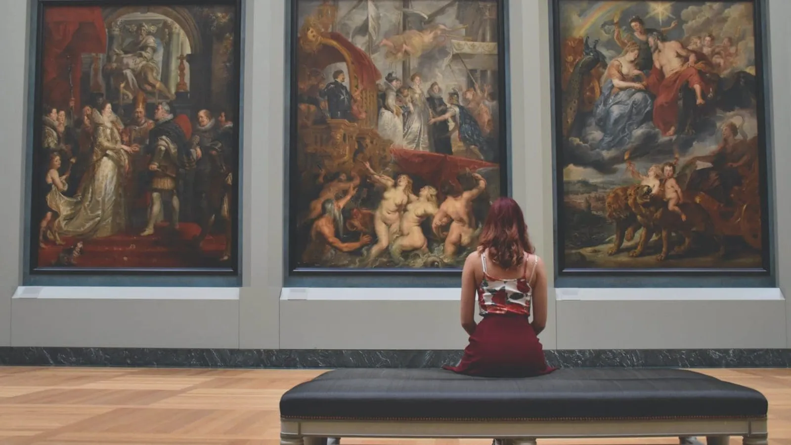 woman sitting on ottoman in front of three paintings