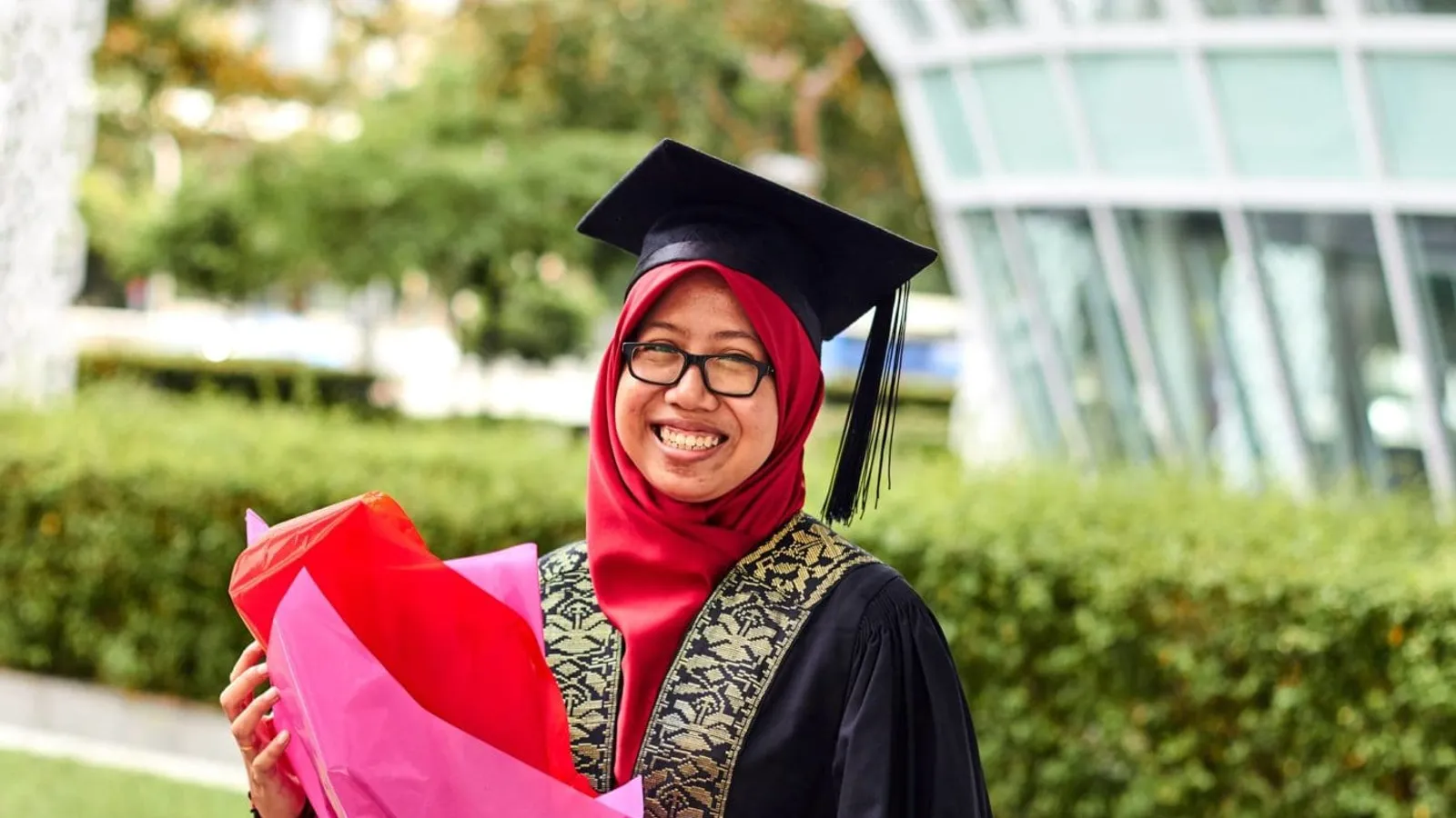 woman wearing academic dress while holding flowers