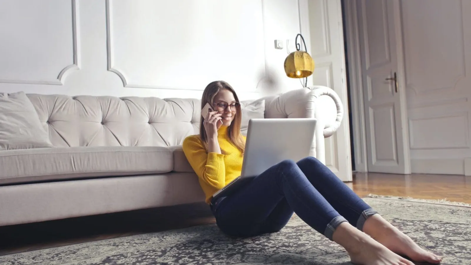 happy adult woman talking on phone and using laptop while chilling at home