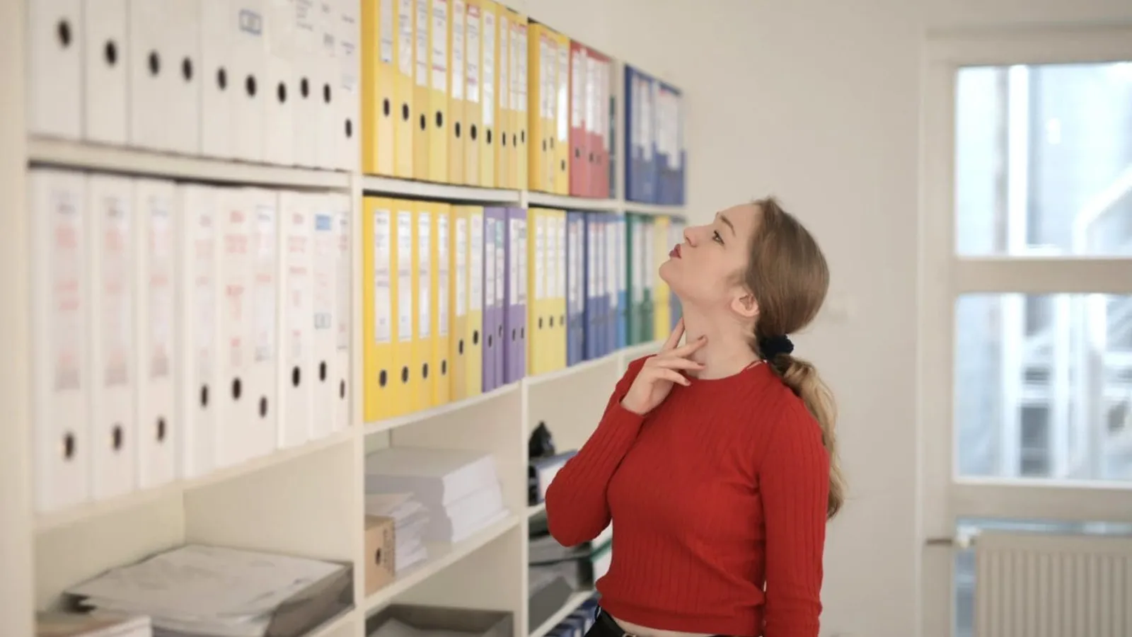 pensive female worker choosing folder with documents in modern office