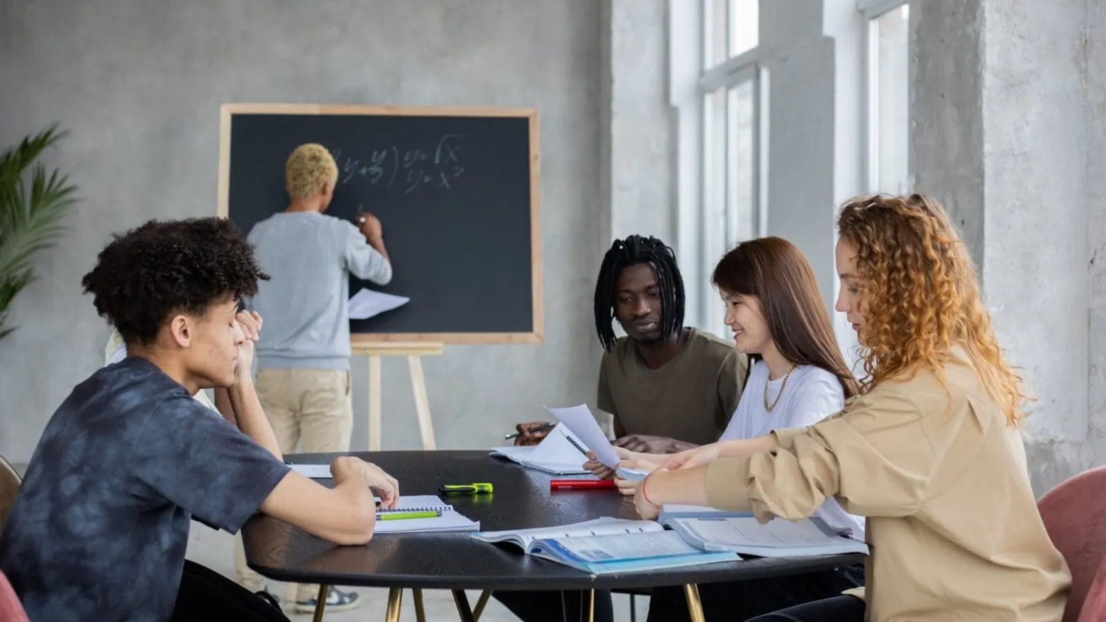 anonymous man writing on chalkboard near group of diverse students at table