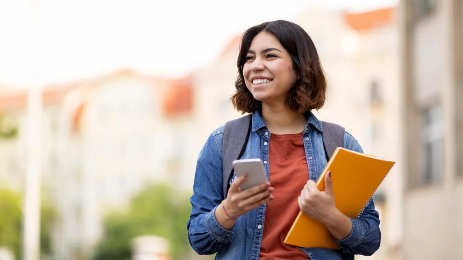 Cheerful,Female,Student,With,Smartphone,And,Workbooks,Standing,Outdoors,