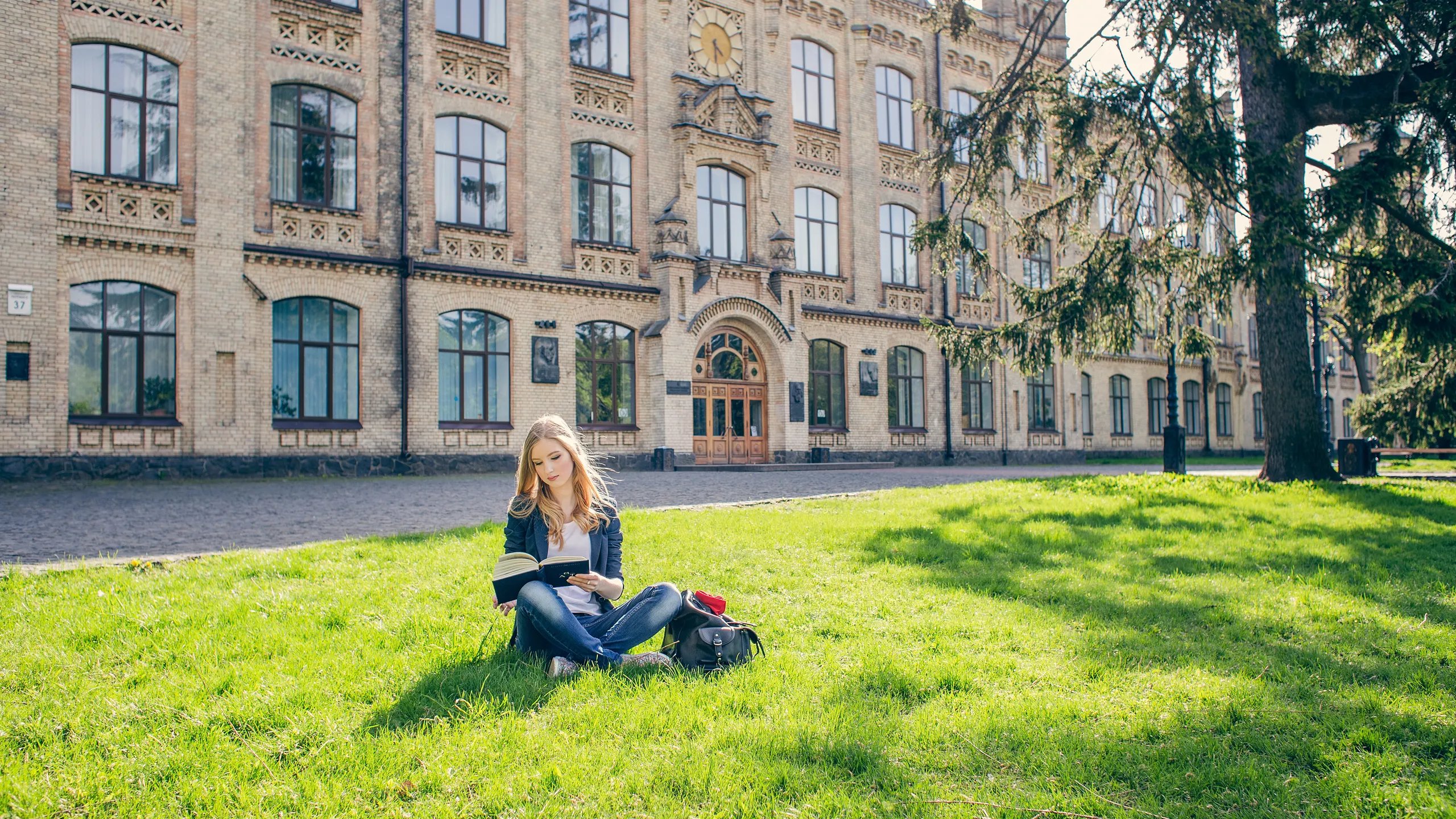 student reading on the grass of a college campus